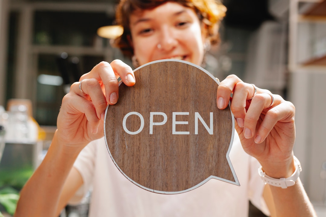 Preencabezado - señora con un cartel de madera de Open
