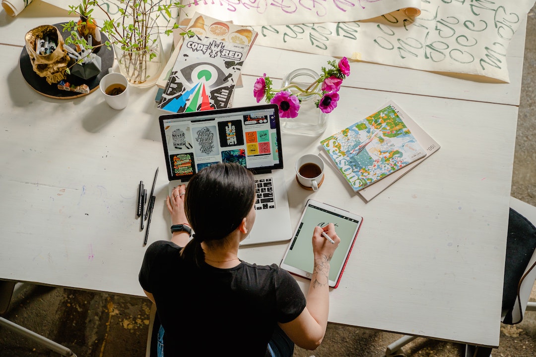 Mujer delante de una mesa con material artístico y ordenador. Foto de Antoni Shkraba - Pexels